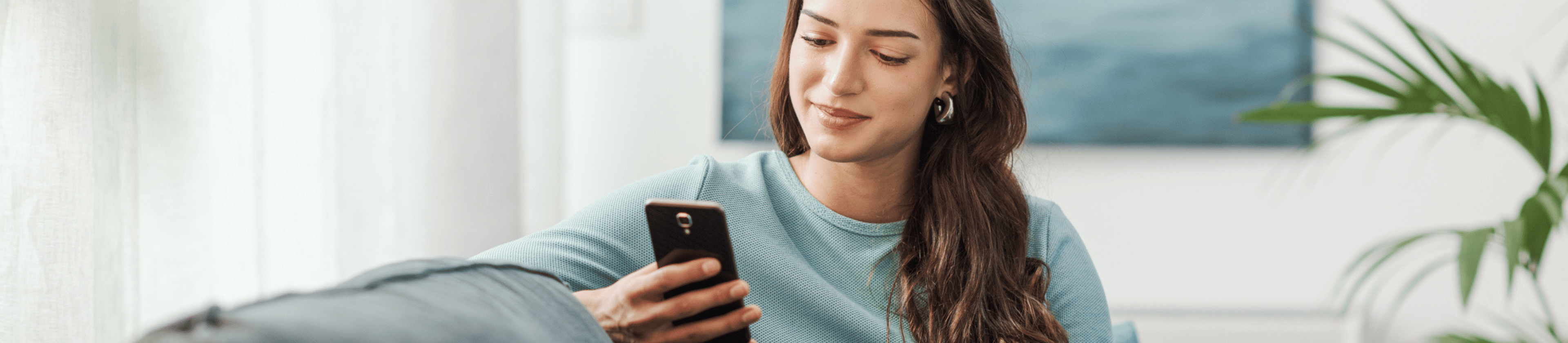 Young woman with long brown hair, wearing blue jumper looking at mobile phone