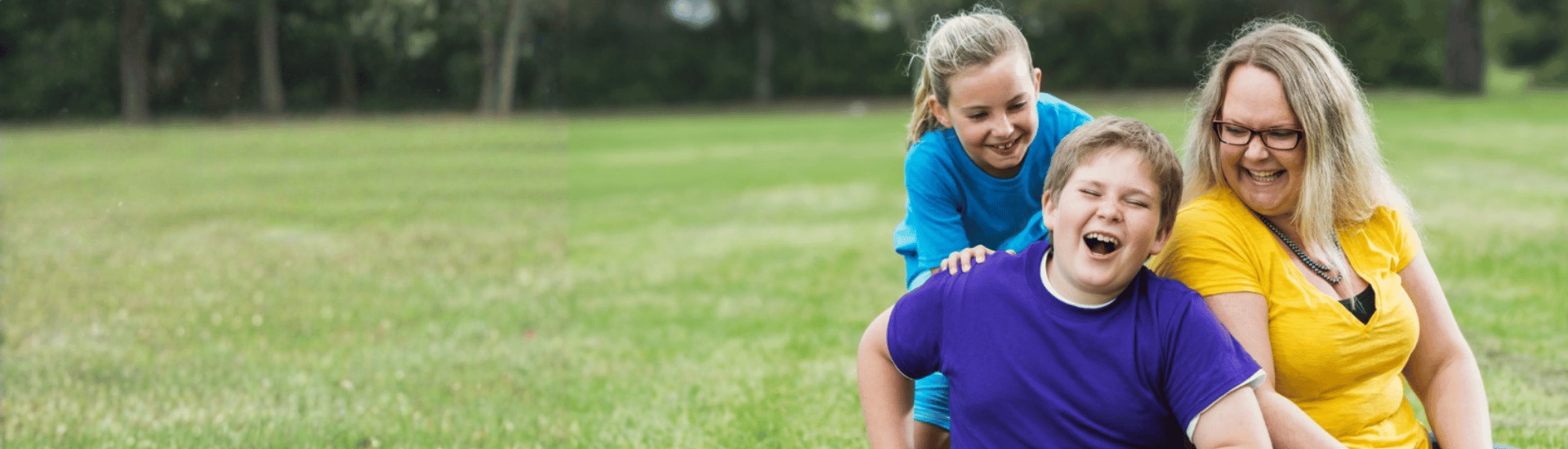 Woman with young boy and young girl smiling while sitting on grass lawn